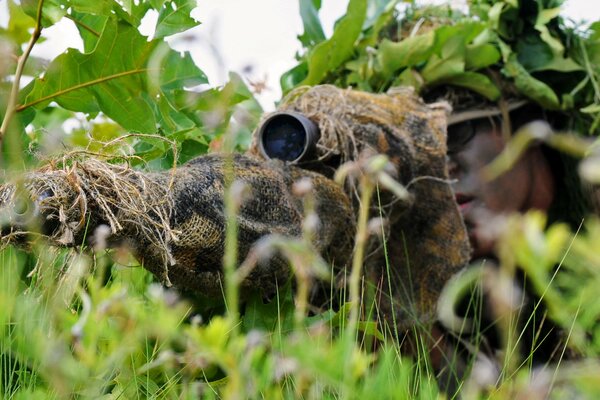 Francotirador disfrazado con rifle en la hierba