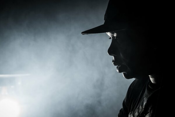 A black man in a hat against the background of smoke and phonor