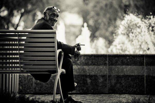 A man sits on a bench and slowly finishes a cigarette