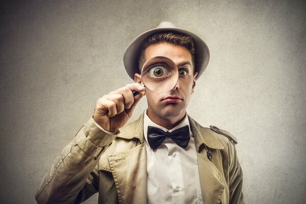 A man in a hat looks through a magnifying glass