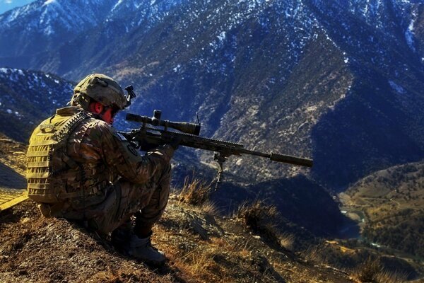 A military sniper is sitting in the mountains