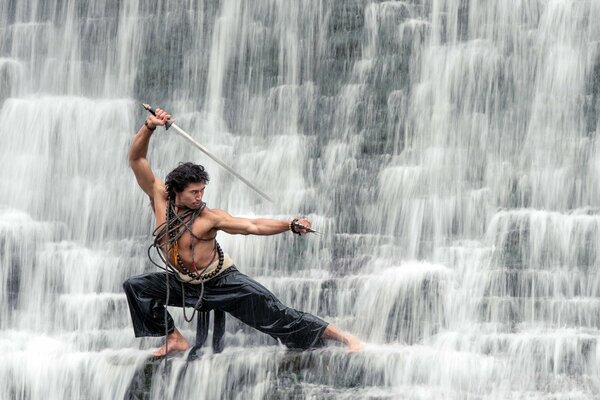 Mann am Wasserfall mit Säbel zeigt Kung Fu