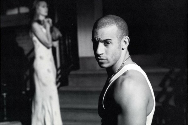 Vin diesel est debout dans le profil et en regardant la caméra sur fond de femme debout