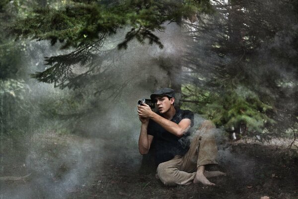 Ein junger Fotograf sitzt barfuß auf dem Boden in einem nebligen Nadelwald und fotografiert