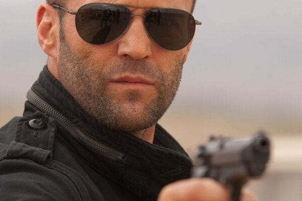 Jason Statham wearing glasses with a gun