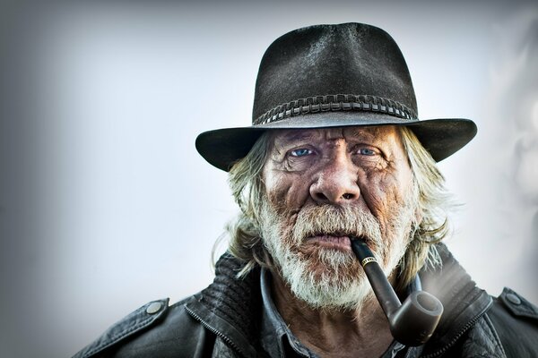 An old man with a pipe in his mouth and a hat