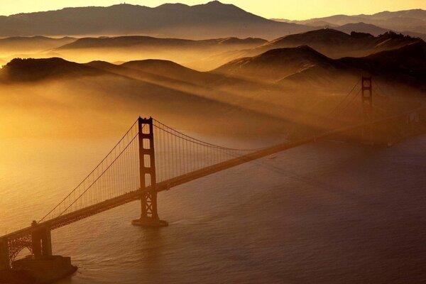 The bridge over the bay unites two shores, beautiful mountains can be seen in the fog