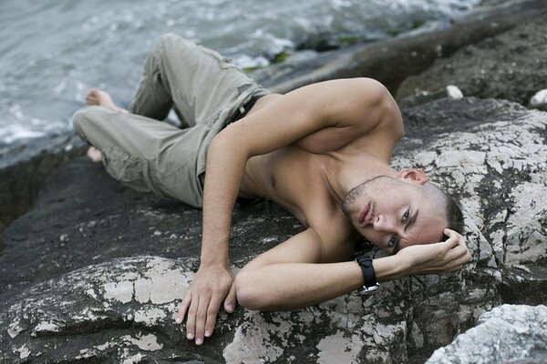 Hombre posando en una piedra junto al agua