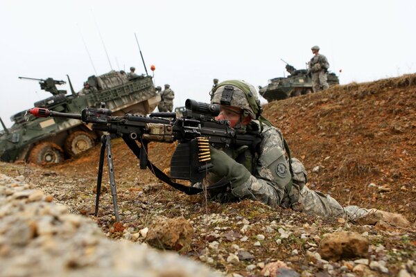 A soldier takes aim against the background of armored personnel carriers