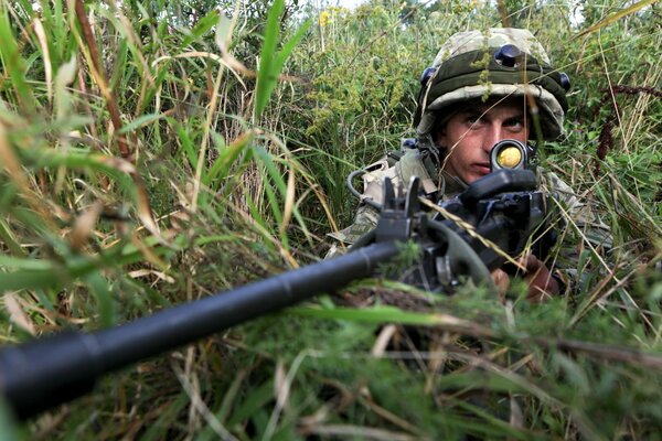 A sniper in camouflage is sitting in ambush