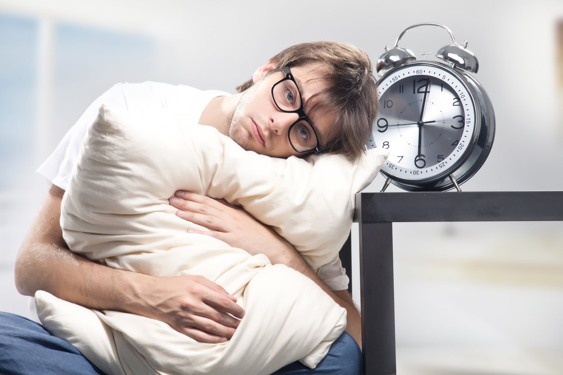 hombre gafas somnoliento descontento almohada reloj despertador seis de la mañana