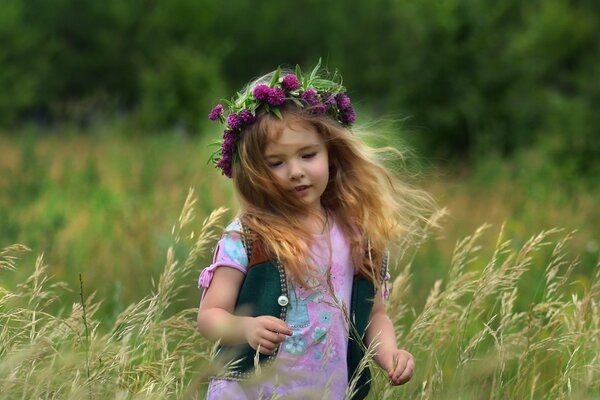 A girl in a wreath runs across the field. Summer landscape