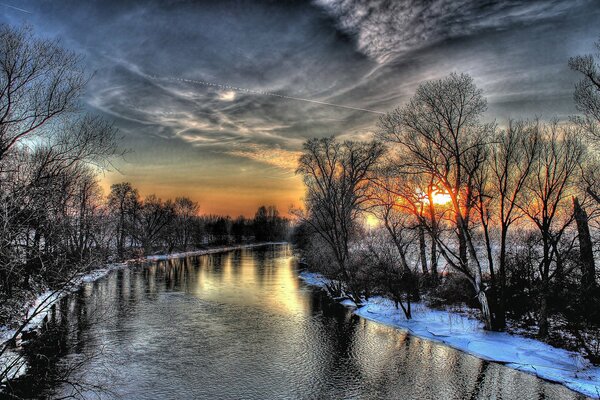 Puesta de sol de invierno en medio de árboles, ríos con nieve