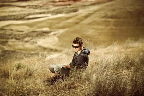 The guy is sitting in a field among the grass