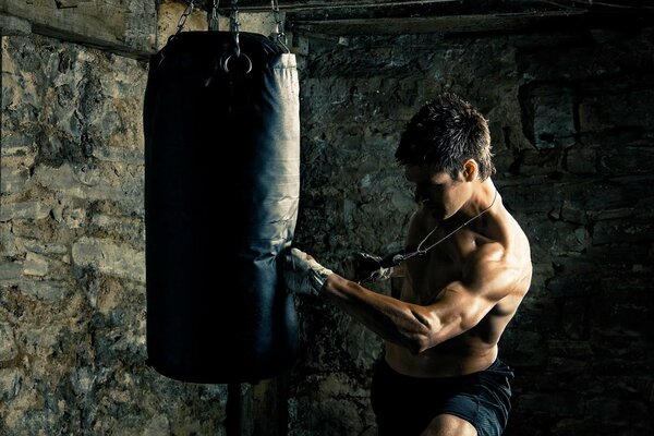 The guy trains his muscles with a punching bag