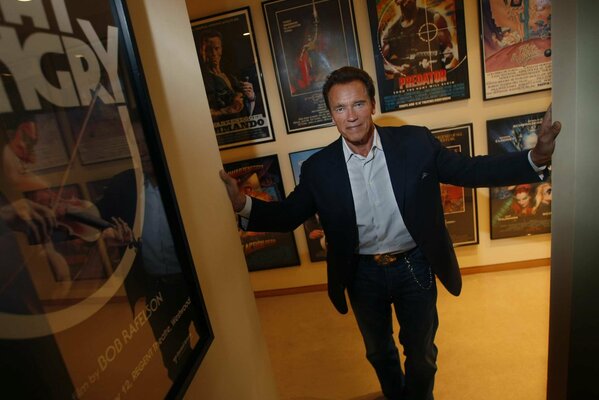 Arnold Schwarzenegger stands on the background of posters