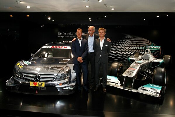 Schumacher y dos hombres de pie junto a dos coches