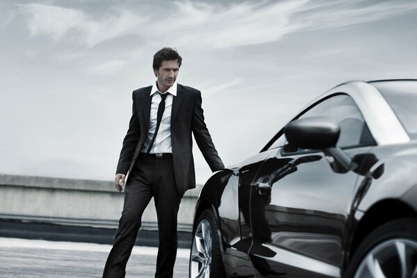 A man in a business suit next to a luxury car