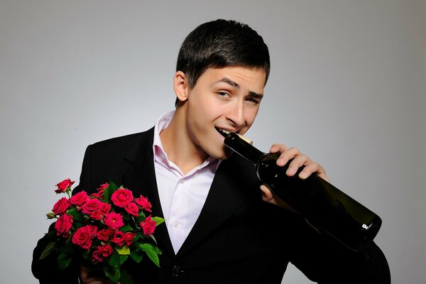 Un giovane carino con un bouquet in mano beve vino da una bottiglia