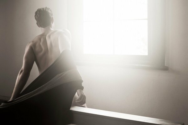 The naked back of a man on the background of a window