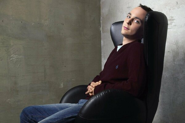 The actor is sitting on a chair in a gray room