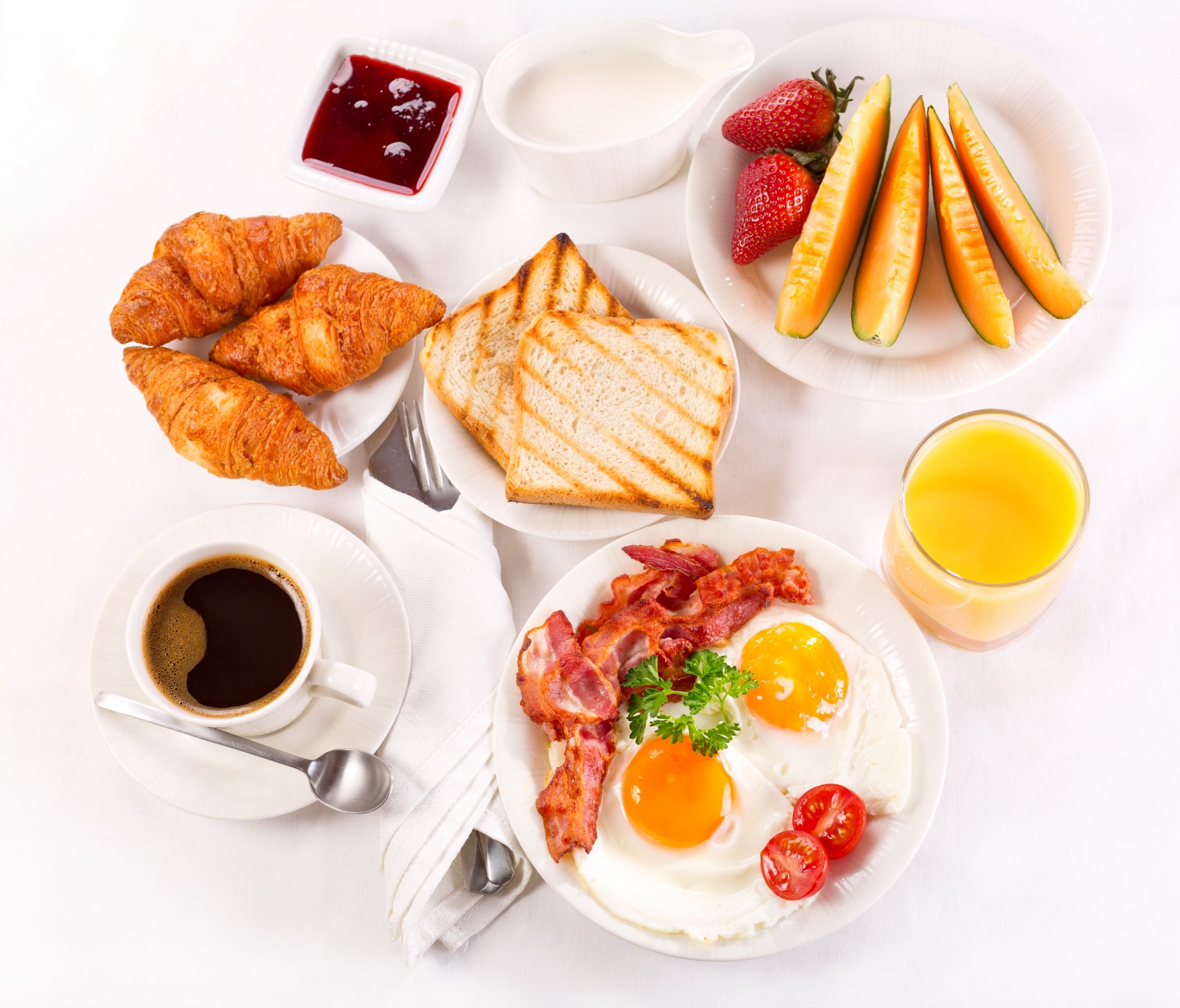 desayuno café taza croissants bandeja fresas jugo mermelada crema tostadas fruta huevos revueltos tocino