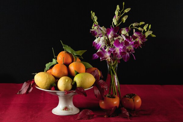 A vase with fruits and flowers standing next to it