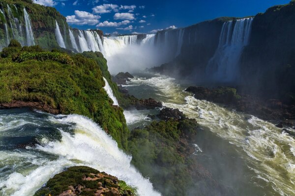 A tropical waterfall with a spray cloud on the background of the sky