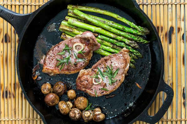 Viande dans une poêle avec des asperges et des champignons