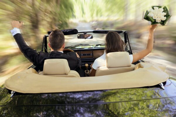 A guy in a suit and a girl with a bouquet are racing in a convertible