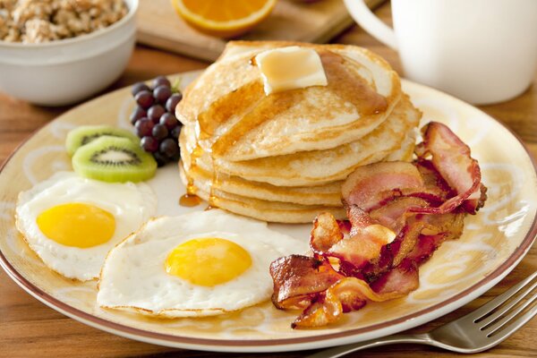 En un plato huevos revueltos, buñuelos, tocino y fruta