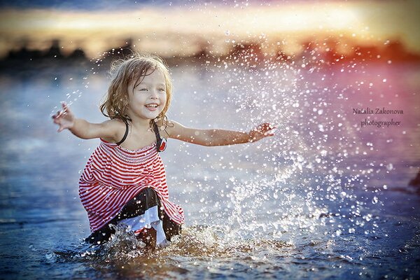 Bambina che gioca in acqua. Tramonto sulla riva