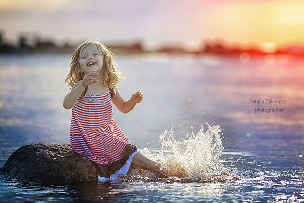 Fille éclaboussant sur le rivage. Coucher de soleil sur l eau