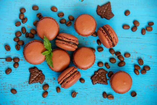 Macarrones de chocolate, galletas de chocolate, granos de café y ramitas de menta sobre un fondo turquesa