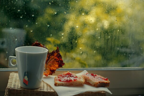 Eine Tasse Tee mit süßen Sandwiches am Fenster