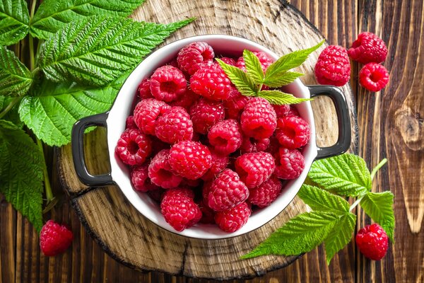 Schönes Foto von Himbeerbeeren mit Blättern auf einem Holzsubstrat