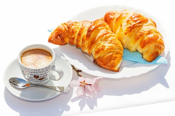 Tasse Kaffee auf einer Untertasse mit einem Löffel und Croissants auf einem Teller