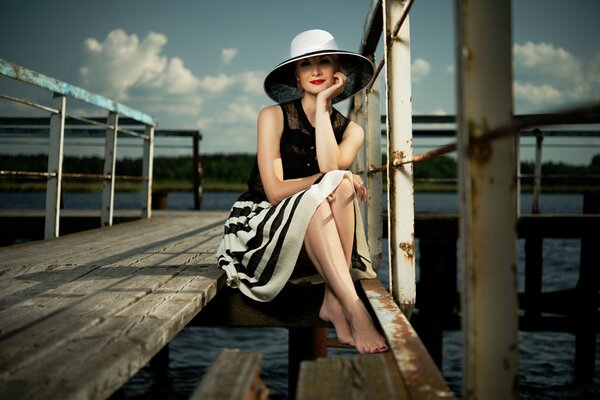 The girl in the hat sitting on the pier