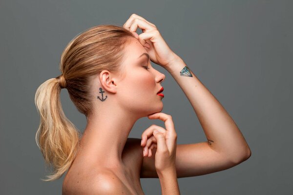 A girl in profile with a tattoo on her wrist with a diamond and on her neck with an anchor