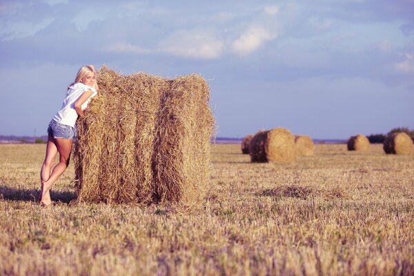 A girl in a field by a haystack