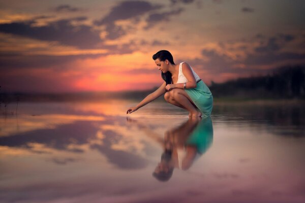 Chica toca la superficie del agua del lago al atardecer