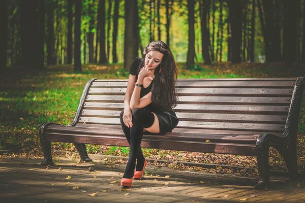 A girl in stockings and a dress in the park on a bench