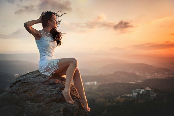 A girl is sitting on a rock in a white dress