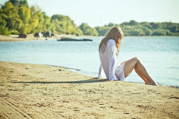 Chica joven sentada en la arena en la playa junto al mar