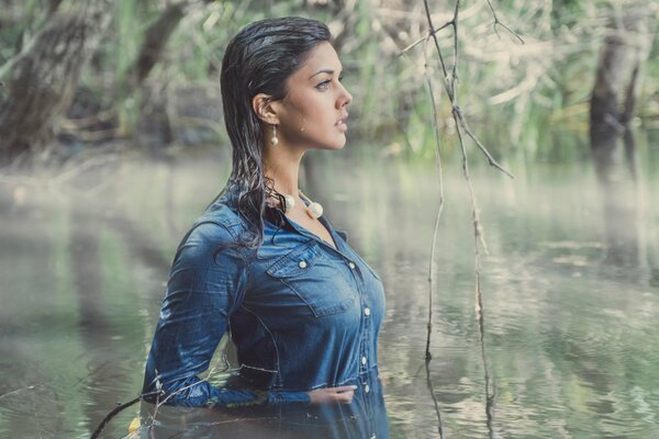 A girl in a blue dress is standing waist-deep in water