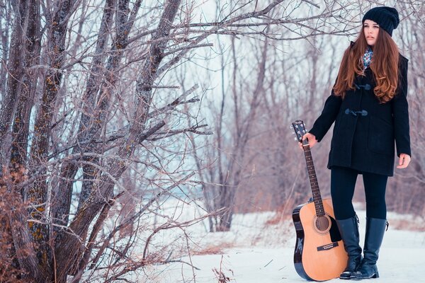 A girl with a guitar in a winter forest