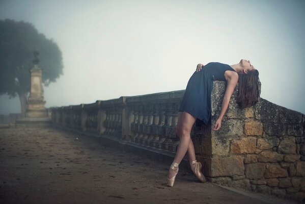 The ballerina is resting, leaning back on the railing