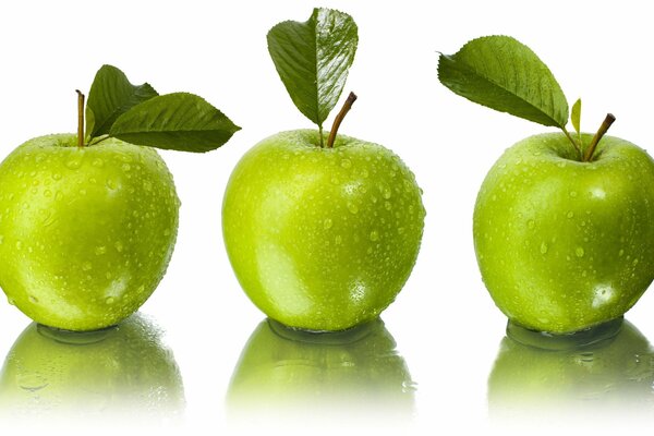 Three green apples are reflected in the water