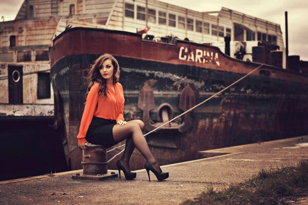 A beautiful girl is sitting on the background of a ship