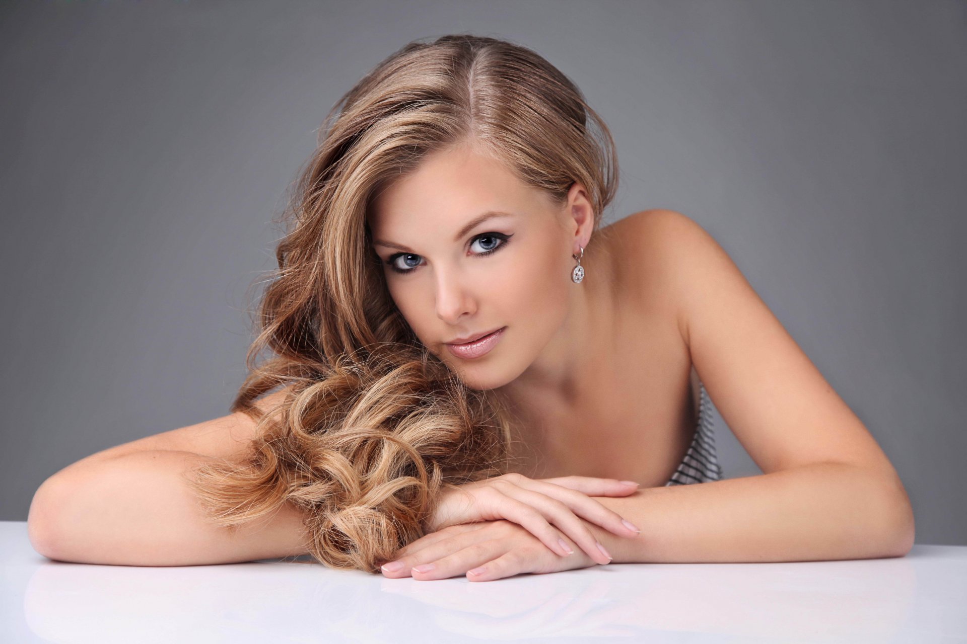 chica rubia cara mirada pelo rizos pendientes maquillaje flechas manos fondo gris